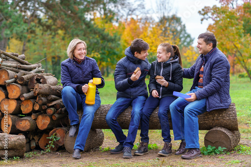 family relaxing outdoor in autumn city park, happy people together, parents and children, they drink tea and eat sandwiches, talking and smiling, beautiful nature © soleg