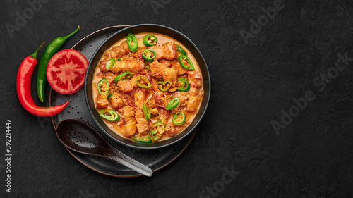 Bicol Express Stew in black bowl on dark slate table top. Filipino cuisine spicy pork belly coconut milk curry. Asian food. Copy space. Top view