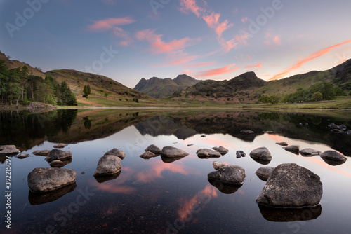 Obraz na plátně Perfect reflections of a beautiful sunrise with scattered rocks in foreground at Blea Tarn in the Lake District, UK