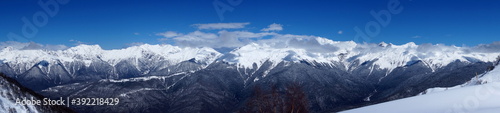 Winter landscape in the mountains. Snow-capped mountain peaks, blue sky, ski slopes.