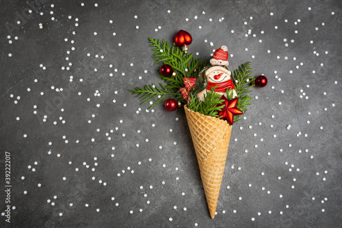 Snowman, thuja twigs and Christmas toys in a waffle cone. Dark gray background with snowflakes. An original sweet gift. Christmas card.