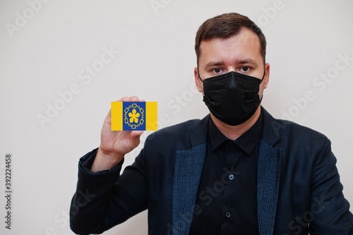 Man wear black formal and protect face mask, hold Hamilton flag card isolated on white background. Canada cities coronavirus Covid concept. photo