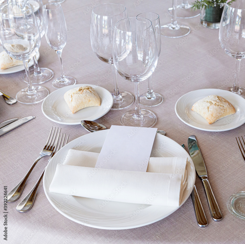 Detail of a beautiful wedding table with crockery, cutlery and wine glasses with a blank menu paper for mock up Detail of a beautiful wedding table with crockery, cutlery and wine glasses with a blank menu paper for mock up