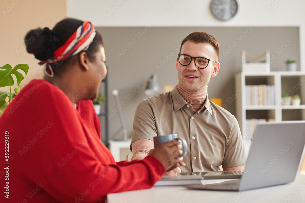 Two young colleagues sitting at the table and working on laptop together in team during meeting at office Two young colleagues sitting at the table and working on laptop together in team during meeting at office