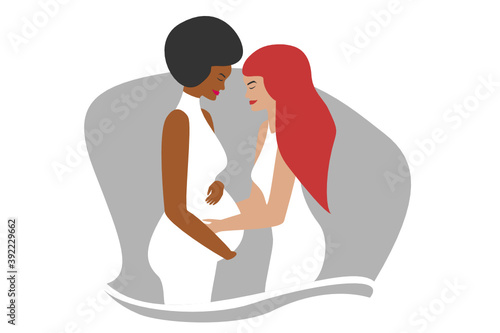 Beautiful female interracial lesbian couple expecting a child. Pregnant african woman and caucasian redhead women in white dresses touching the belly being happy