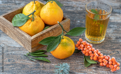 Fresh tangerines with leaves in a box, mint tea and sea buckthorn on a wooden rustic background