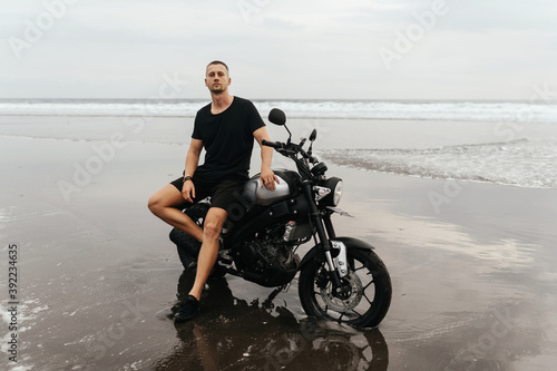 Close up portrait of biker at beach of Bali Indonesia. Handsome man sitting on handmade vintage recast motorcycle