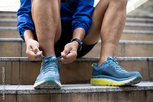 Fototapeta Naklejka Na Ścianę i Meble -  Close-up, a man in a blue Windbreaker jacket laces his shoes to sneakers on the stairs., Training begins.