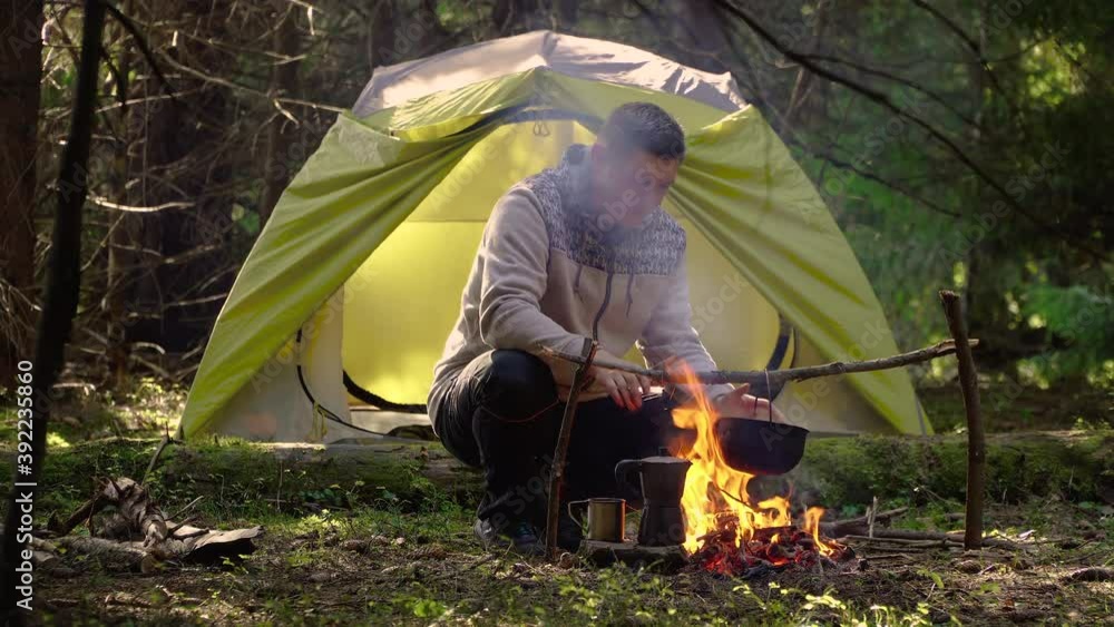 The man sits near the fire. Camping in a beautiful forest. The food in the cauldron is cooked over the fire. Travel concept The man sits near the fire. Camping in a beautiful forest. The food in the cauldron is cooked over the fire. Travel concept