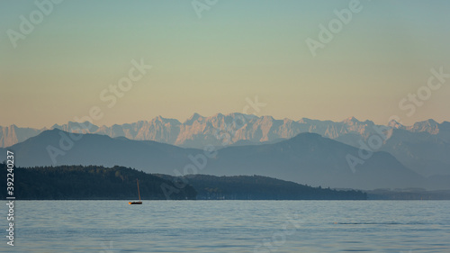 Kleines Segelboot auf dem Starnbeger See bei Bernried in Oberbayern im Sommer bei Sonnenaufgang mit den Alpen im Hintergrund