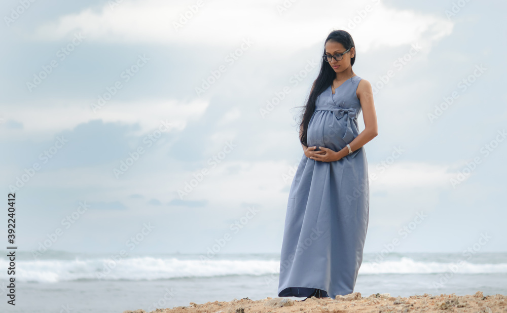 Young pregnant women holding her belly, standing in the beautiful beach, expectations, and mother's love for her unborn child concept. Young pregnant women holding her belly, standing in the beautiful beach, expectations, and mother's love for her unborn child concept.