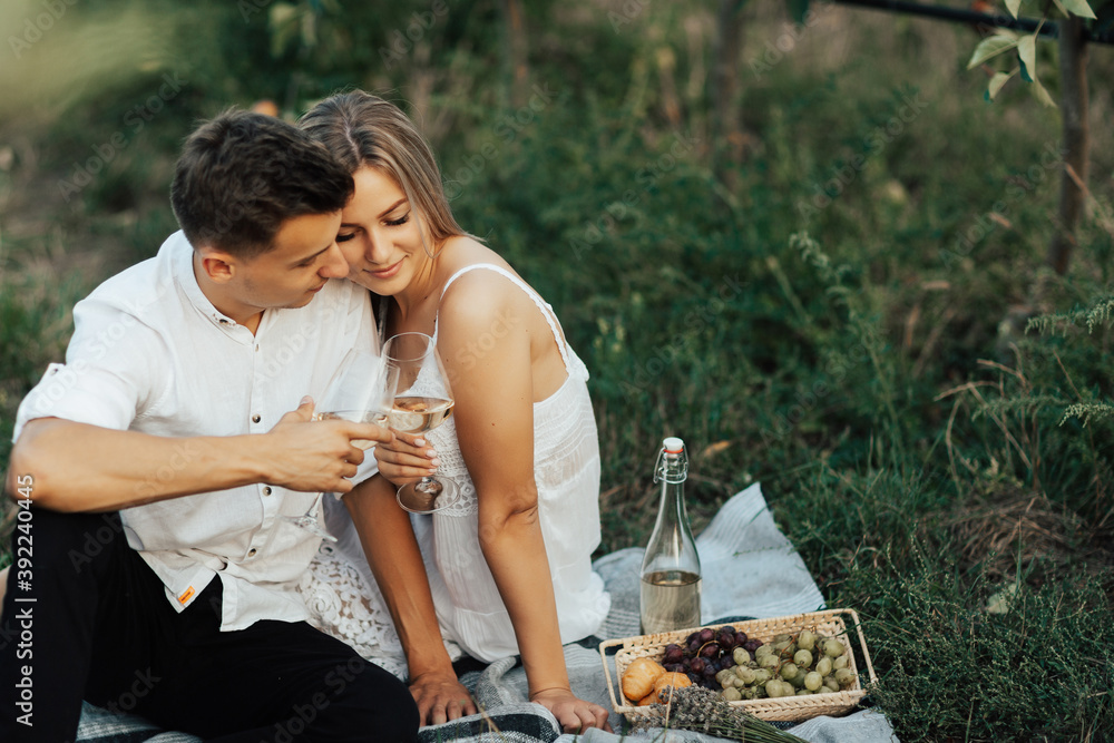 Couple in love drinks a white wine on summer picnic. Young couple is having picnic together in summer park.