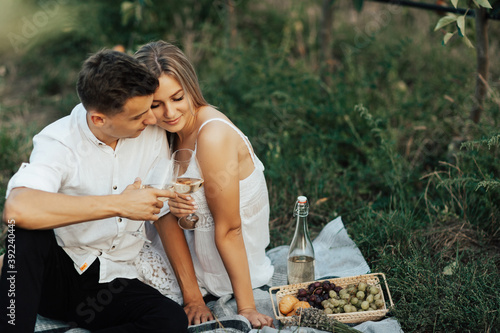 Obraz na płótnie Couple in love drinks a white wine on summer picnic. Young couple is having picnic together in summer park. w salonie