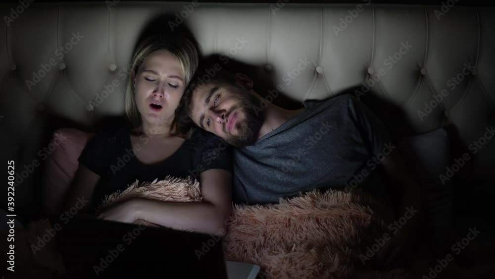 Man and woman, young couple watching boring movie on laptop in bed before bedtime Man and woman, young couple watching boring movie on laptop in bed before bedtime