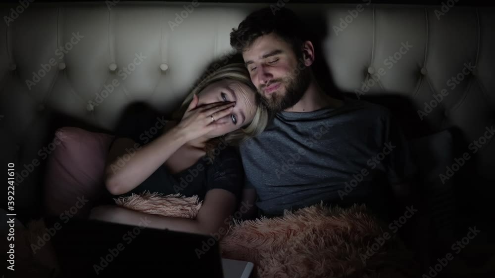 Man and woman, young couple watching boring movie on laptop in bed before bedtime Man and woman, young couple watching boring movie on laptop in bed before bedtime