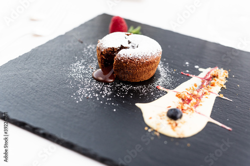 Primo piano di un tortino di cioccolato con cuore caldo accompagnato da crema pasticcera e frutti rossi