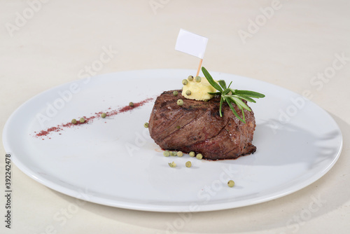 juicy fried minienne meat steak decorated with a slice of butter and a sprig of rosemary with a flag for the logo on a white plate on a white background
