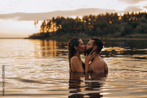 Romantic photo session in the water. A guy and a girl swim in the lake in the evening. Beautiful sunset.