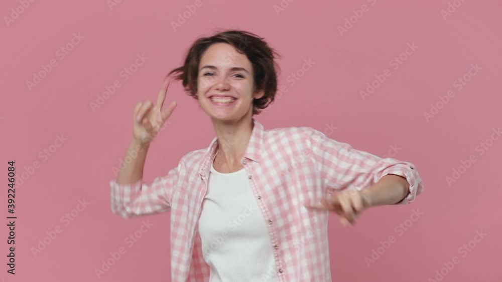 Cheerful funny young woman 20s wearing casual checkered shirt isolated on pink background studio. People lifestyle concept. Dancing waving hands point fingers up clenching fists showing victory sign Cheerful funny young woman 20s wearing casual checkered shirt isolated on pink background studio. People lifestyle concept. Dancing waving hands point fingers up clenching fists showing victory sign