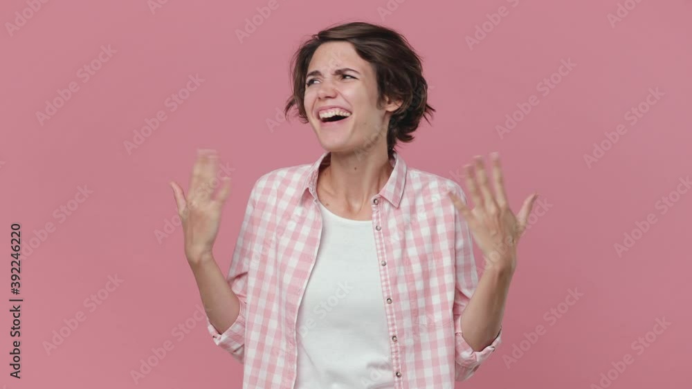 Shocked surprised joyful young brunette woman 20s years old wearing casual checkered shirt posing isolated on pink color background studio. People lifestyle concept. Put hands on chest ask who me