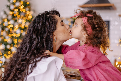 Christmas mood family at home cozy. Mom and daughter mix race oriental kiss. Love parenting childhood. Lifestyle small moments of life. Motherhood together happy offline photo