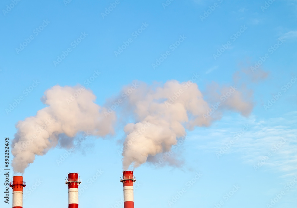 Smoking industrial stacks in thermal power plant emit polluted air into atmosphere in blue sky Smoking industrial stacks in thermal power plant emit polluted air into atmosphere in blue sky