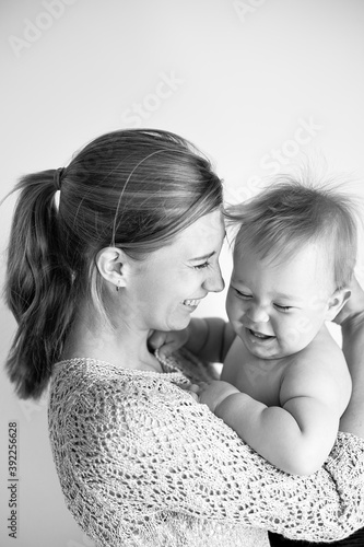 young mom laughs and hugs her son, baby 1 year old, baby care leave, happy motherhood and childhood, black and white photo, selective focus