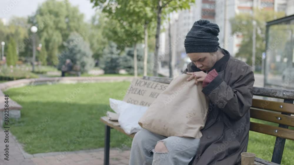 Homeless woman searching for food in dirty bag, sitting on bench, survival Homeless woman searching for food in dirty bag, sitting on bench, survival