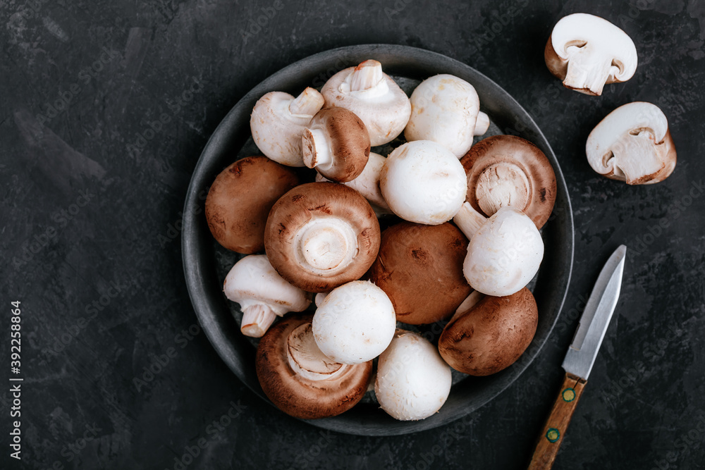 Fresh organic brown and white champignon mushrooms in bowl on dark stone background. Fresh organic brown and white champignon mushrooms in bowl on dark stone background.