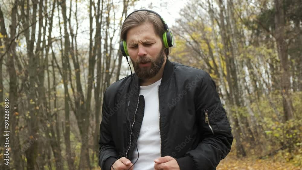 A young brutal Caucasian man is emotionally walking in an autumn park and listening to music on headphones. Dancing and relaxation A young brutal Caucasian man is emotionally walking in an autumn park and listening to music on headphones. Dancing and relaxation