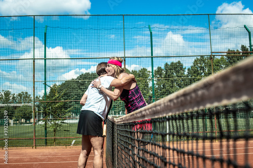 Two active senior Caucasian women in sportswear playing tennis, hugging after the match © TheSupporter
