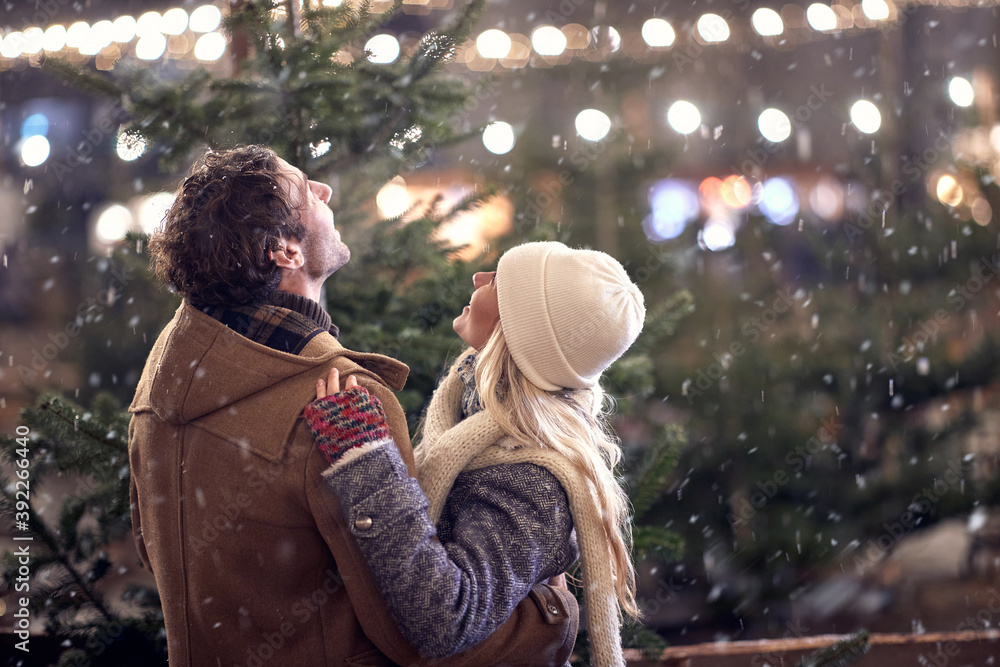 A young couple in hug watching snowflakes in the city. Christmas tree, love, relationship, Xmas, snow