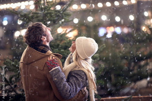 A young couple in hug watching snowflakes in the city. Christmas tree, love, relationship, Xmas, snow