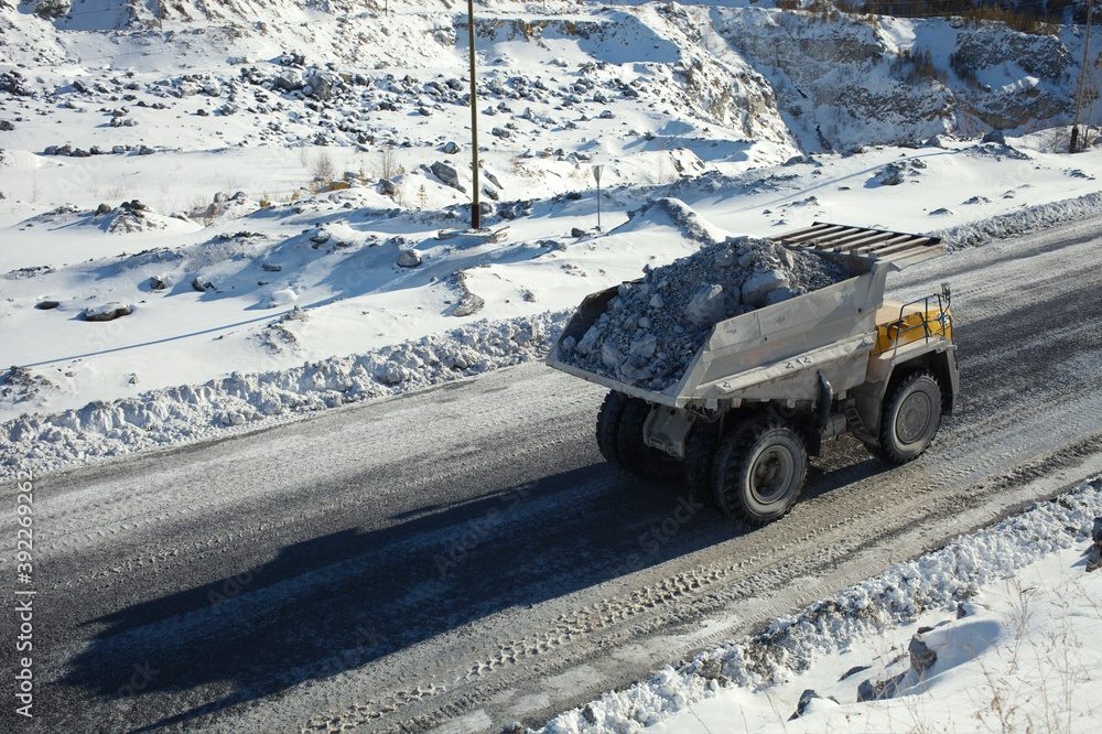 Φωτογραφία Heavy mining truck transports stone ore against the background of a snow-covered quarry in sunny weather, close-up
