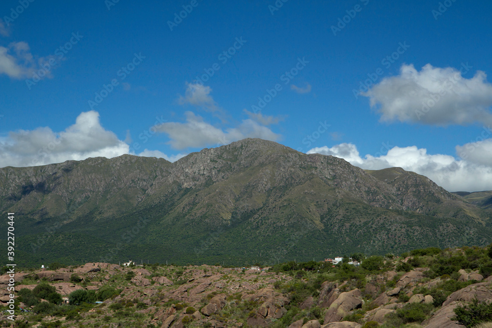 Beautiful view of popular landmark Uritorco hill, valley and green forest under a deep blue sky with clouds in Capilla del Monte, Cordoba, Argentina.