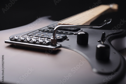 Elegant electric guitar on black background close up point of view showing larger part from body with humbucker pickups to head with silver tremolo and black pickguard and knobs