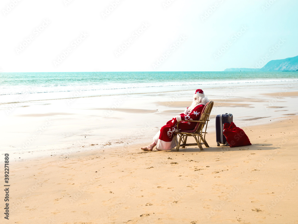 Santa Claus sits on a chair barefoot with a suitcase and a red bag with ...