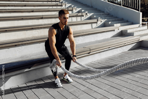 Sporty young man doing fitness workout outdoors, muscular man with chest doing workout using two fighting ropes © Shopping King Louie