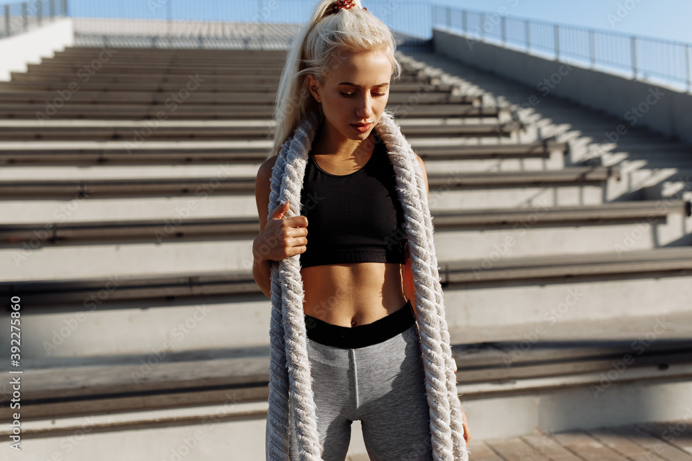 Obraz premium Sportive young confident woman, in sportswear, with fighting ropes, outdoors against the background of the urban summer flyer, sports, motivation