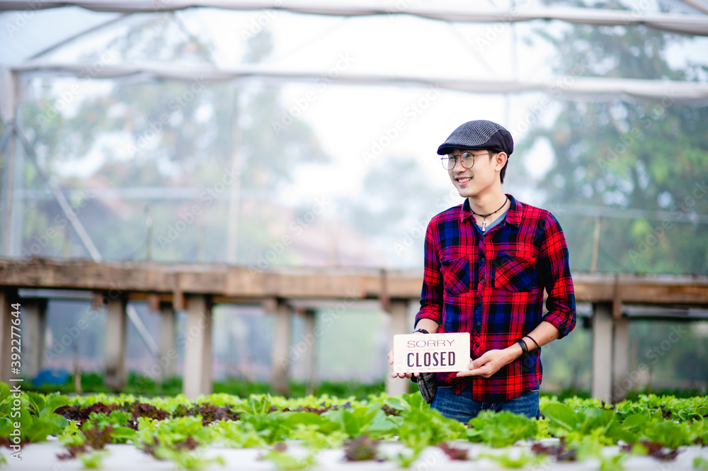 The young man and the shop opening sign welcome to visit his organic vegetable garden. The young man and the shop opening sign welcome to visit his organic vegetable garden.