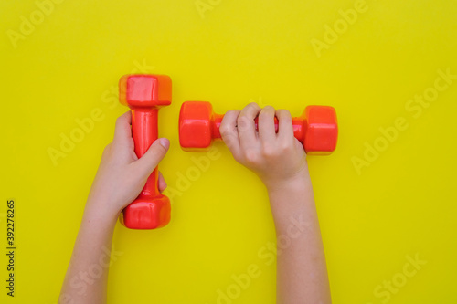 Children's hands hold red dumbbells on a yellow background.