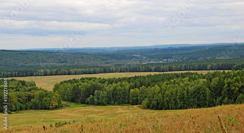 Amazing autumn landscape - view from a hill on a hilly area under a gloomy autumn sky.