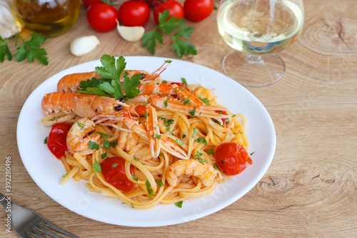 Italian Traditional Dish"Linguine agli Scampi" or "Linguine with Scampi Shirmps",linguine with scampi,cherry tomatoes,white wine,olive oil,parsley,garlics and peppers on white plate with wooden table