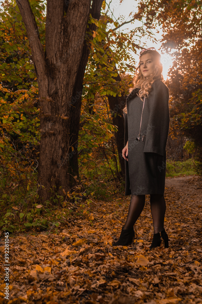 A happy adult girl in a black cloak stands in chameleon glasses in autumn. Yellow forest, green grass, blonde. looking at camera comparison concept