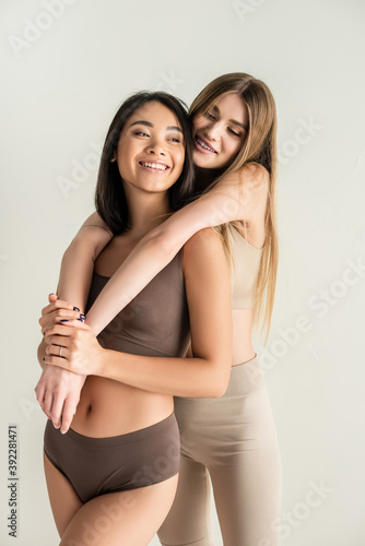 blonde woman hugging happy asian model while posing isolated on white © LIGHTFIELD STUDIOS