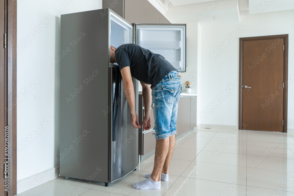 Op een warme dag koelt de man af met zijn hoofd in de koelkast. Kapotte  airconditioner #392282076 - Hout