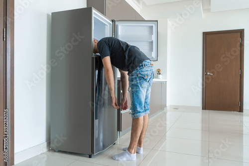 Murais de parede On a hot day, the guy cools with his head in the refrigerator
