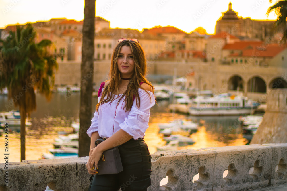 Φωτογραφία Fashionable attractive brunette posing on the city walls of Dubrovnik city as the sun sets during the golden hour