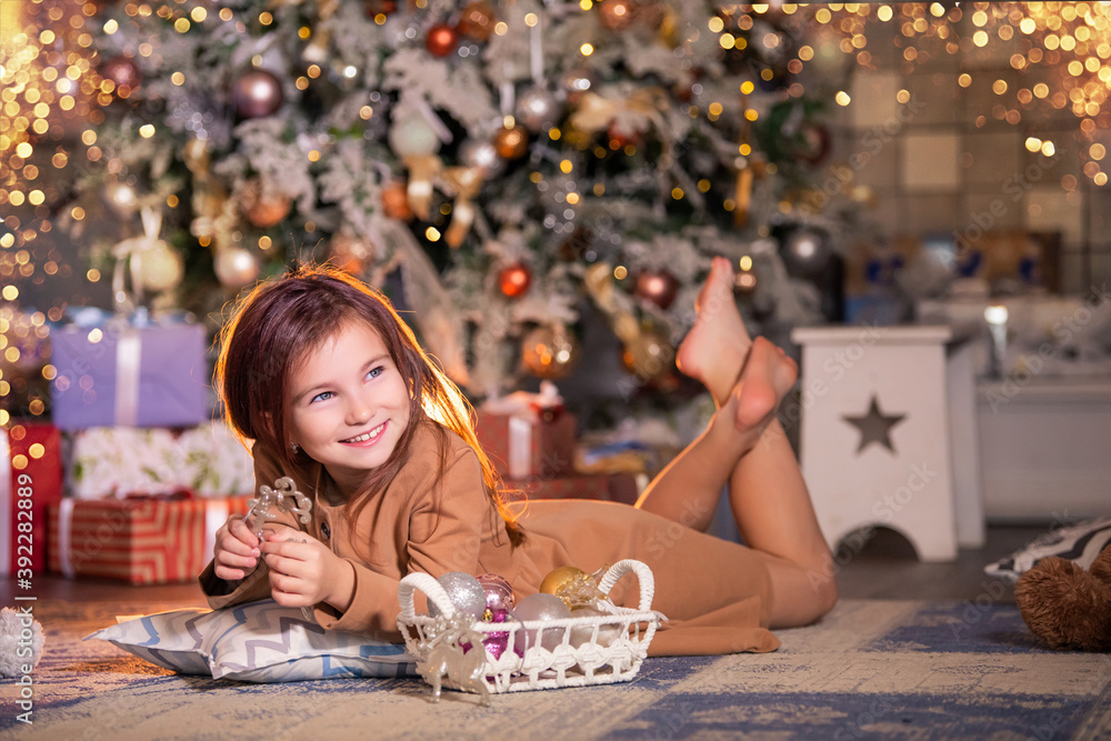happy girl lies on the floor against the background of Christmas tree and holds deer Christmas decoration in her hands. happy girl lies on the floor against the background of Christmas tree and holds deer Christmas decoration in her hands.
