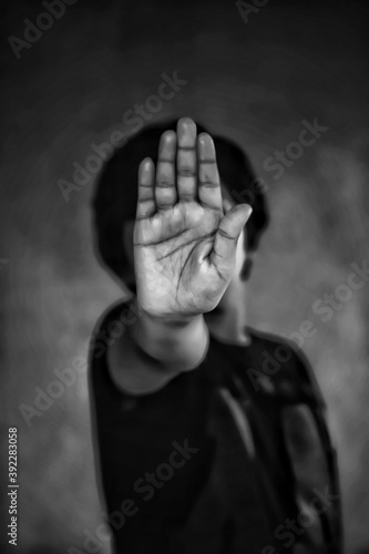 A black and white photo of a young boy hiding his face with his hand and asking to stop